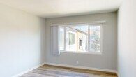 Located at 6233 S La Brea Ave in Los Angeles, CA, this well-appointed 1-bedroom, 1-bathroom single-floor unit offers a clean, modern aesthetic throughout. Light wood-style flooring runs consistently across every room, complementing the soft grey and white wall palette that creates a bright, cohesive atmosphere.

The living room is an open, airy space anchored by a large sliding window that fills the room with natural light and offers views of the surrounding neighborhood. A separate dining area sits adjacent, featuring its own window and a pendant light fixture overhead, with easy sight lines into the bedroom and hallway beyond.

The kitchen is compact yet functional, equipped with dark shaker-style cabinetry, a white countertop, and a stainless steel double-basin sink positioned beneath a bright window. A glass-paneled exterior door provides additional light and outdoor access.

The bedroom offers a comfortable, well-proportioned layout with a ceiling fan, a large window framing lush greenery outside, and a mirrored sliding-door closet with built-in upper cabinetry for added storage.

The bathroom features a clean, all-white design with a stone-look countertop, a modern single-lever faucet, a large mirror, and a full-size soaking tub with a shower, accented by brushed nickel fixtures throughout.