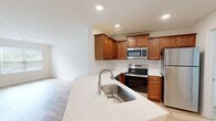Located at 1000 Avonlea Pl in Woodstock, GA, this single-floor, 2-bedroom, 1-bathroom home offers a thoughtfully designed open layout. The combined kitchen and living area serves as the heart of the home, featuring warm medium-toned wood cabinetry, stainless steel appliances including a refrigerator, range, microwave, and dishwasher, and a peninsula with a white quartz-style countertop and undermount sink. Light hardwood-style flooring runs throughout the main living areas, complementing the bright, neutral color palette. Large windows in the living area allow generous natural light and offer views of the surrounding greenery, with a glass door providing direct outdoor access. The hallway leads to two carpeted bedrooms, each with natural light; the primary bedroom includes a ceiling fan and a sizable window with outdoor views. The full bathroom is finished with warm wood cabinetry, a wide vanity with ample storage, and a large wall mirror. Multiple closets provide excellent storage throughout. A dedicated laundry area with washer/dryer hookups and built-in wire shelving adds everyday convenience. A pantry and utility room further enhance the functional design of this well-appointed Woodstock home.