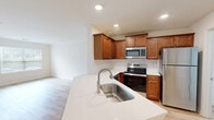 Located at 1000 Avonlea Pl in Woodstock, GA, this single-floor, 2-bedroom, 1-bathroom home offers a thoughtfully designed open layout. The combined kitchen and living area serves as the heart of the home, featuring warm medium-toned wood cabinetry, stainless steel appliances including a refrigerator, range, microwave, and dishwasher, and a peninsula with a white quartz-style countertop and undermount sink. Light hardwood-style flooring runs throughout the main living areas, complementing the bright, neutral color palette. Large windows in the living area allow generous natural light and offer views of the surrounding greenery, with a glass door providing direct outdoor access. The hallway leads to two carpeted bedrooms, each with natural light; the primary bedroom includes a ceiling fan and a sizable window with outdoor views. The full bathroom is finished with warm wood cabinetry, a wide vanity with ample storage, and a large wall mirror. Multiple closets provide excellent storage throughout. A dedicated laundry area with washer/dryer hookups and built-in wire shelving adds everyday convenience. A pantry and utility room further enhance the functional design of this well-appointed Woodstock home.