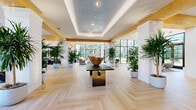 Silversaw is a beautifully designed single-floor communal space that seamlessly blends nature-inspired aesthetics with modern architecture. Throughout the space, light-toned herringbone hardwood flooring creates a warm, cohesive foundation, while exposed natural timber beams accent the soaring ceilings above. Abundant floor-to-ceiling black-framed windows and glass doors flood the interiors with natural light and offer lush outdoor views, reinforcing the space's strong biophilic identity.

The reception area features a sleek white quartz counter with light wood accents, a vibrant botanical mural, and trailing greenery overhead, setting an inviting first impression. Dozens of large potted tropical plants are positioned throughout, enhancing the organic atmosphere.

Multiple distinct lounge areas are thoughtfully arranged across the open floor plan. One features a striking suspended copper fireplace encircled by curated seating, while another showcases a live moss accent wall paired with a large display screen and modular sofa seating. A spacious social lounge offers oversized sectional sofas beneath dramatic double-height windows. The kitchen and bar area includes a generous white marble island, custom cabinetry, and designer pendant lighting. Private office suites with glass partitions are also available, completing this versatile and visually compelling space.