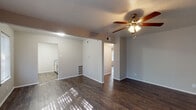 This single-floor residence offers a clean, functional layout with consistent dark hardwood-style flooring running throughout every room, creating a cohesive and polished aesthetic. The living area is generously proportioned, bathed in natural light streaming through large windows fitted with horizontal blinds. A ceiling fan with a built-in light fixture provides both comfort and illumination, while neutral gray walls lend a calm, versatile backdrop. The space opens toward the kitchen, offering an easy flow between the living and cooking areas. The galley-style kitchen is well-equipped with gray cabinetry on both sides, speckled laminate countertops, a white appliance suite including a range, refrigerator, dishwasher, and microwave, and a classic white subway tile backsplash with a stainless steel double sink. The bedrooms are comfortably sized with large windows that invite natural light and feature multiple bi-fold closet doors, providing generous storage capacity. The bathroom is finished with large-format gray tile surrounding a soaking tub and shower combination, complemented by a vanity with a speckled countertop and wood-style flooring. Throughout the space, the neutral color palette and consistent finishes contribute to a tidy, move-in-ready atmosphere.