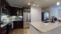 This well-designed single-floor residence offers a thoughtfully laid-out living experience with modern finishes throughout. The open-concept kitchen serves as the heart of the home, showcasing rich dark cabinetry that extends floor to ceiling, stainless steel appliances including a French door refrigerator and over-the-range microwave, and a striking herringbone-patterned tile backsplash. A large granite-topped island with an undermount sink provides ample workspace and acts as a natural transition into the main living areas. Warm hardwood-style flooring flows throughout the main living spaces, complemented by pendant lighting over the island and track lighting in the kitchen.

The living room is bright and welcoming, featuring a ceiling fan, natural light from multiple windows, and direct access to an exterior door. The bedrooms offer plush carpeting and ceiling fans, with one room featuring a spacious, flexible layout ideal for various configurations. The bathroom is finished with large-format tile in the shower and tub surround, a granite-topped dark vanity, and direct access to a built-in walk-in closet with ample shelving. Together, these spaces create a cohesive, contemporary residence with practical, high-quality finishes throughout.