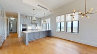 Located in the heart of Jacksonville, FL, this thoughtfully designed one-bedroom, three-bathroom residence offers a generous and open single-floor layout. The expansive living room is immediately impressive, featuring soaring ceilings, whitewashed exposed brick walls, wide-plank light oak hardwood floors, and a striking multi-arm Edison bulb chandelier. Large black-framed windows flood the space with natural light while framing sweeping panoramic views of the Jacksonville skyline and waterfront.

The open-concept kitchen is a standout feature, showcasing custom soft-gray shaker cabinetry with brass hardware, a large quartz waterfall island with a farmhouse sink, stainless steel double wall ovens, a professional range hood, and pendant lighting with gold-toned interiors. The kitchen flows seamlessly into the living area, making it ideal for entertaining.

The bedroom offers hardwood flooring, generous natural light, and built-in cabinetry with shelving. Each of the three bathrooms is finished with marble tile flooring, marble-surround glass-enclosed walk-in showers, elegant vanities with brass fixtures, and refined wall sconces, creating a spa-like atmosphere throughout. The overall ambiance is clean, modern, and sophisticated.