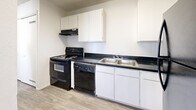 This single-floor unit is laid out with a practical and straightforward design, finished throughout in crisp white walls and neutral tones that lend a clean, move-in-ready aesthetic. The kitchen is well-equipped, featuring black appliances including an electric range, dishwasher, and refrigerator, paired with white cabinetry and dark speckled countertops that provide a classic contrast. Light wood-look flooring runs through the kitchen and entry areas, adding warmth underfoot.

The living area is carpeted and benefits from a wide bank of windows dressed with vertical blinds, allowing natural light to filter in while a wall-mounted HVAC unit provides climate control. A half-wall partition defines the transition between the living and entry spaces, with a set of large bi-fold closet doors nearby offering generous storage.

The bedrooms are carpeted and simply appointed, each featuring bi-fold closet doors and windows that bring in additional natural light. Wall-unit heaters are present in at least one bedroom, ensuring individual climate comfort.

The bathroom is clean and functional, featuring dark speckled countertops atop white cabinetry, a medicine cabinet with mirror, and a separate shower stall alongside a full soaking tub. Textured ceilings appear throughout, adding a subtle architectural consistency to the space.