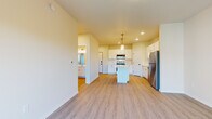 This single-floor unit is designed with a clean, modern aesthetic throughout, characterized by light-toned luxury vinyl plank flooring, crisp white walls, and recessed lighting that create a bright and cohesive atmosphere.

The kitchen serves as a central feature of the space, showcasing white shaker-style cabinetry, white countertops, and a subway tile backsplash. Stainless steel appliances — including a range, over-the-range microwave, refrigerator, and dishwasher — provide a polished, functional finish. A center island with a white countertop offers additional workspace and serves as a natural gathering point, while pendant lighting above adds a refined touch. Recessed ceiling lights further illuminate the area.

The living area is open and generously proportioned, with a sliding glass door leading to a private balcony that overlooks mature trees, bringing in natural light and outdoor views.

The bathroom is well-appointed with a full tub-shower combination, white vanity cabinetry, and black hardware accents. A dedicated laundry area accommodates a full-sized top-load washer and dryer, complemented by wire shelving above for added storage. Additional rooms provide flexible, neutrally finished spaces suitable for various uses.