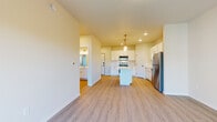 This single-floor unit is designed with a clean, modern aesthetic throughout, characterized by light-toned luxury vinyl plank flooring, crisp white walls, and recessed lighting that create a bright and cohesive atmosphere.

The kitchen serves as a central feature of the space, showcasing white shaker-style cabinetry, white countertops, and a subway tile backsplash. Stainless steel appliances — including a range, over-the-range microwave, refrigerator, and dishwasher — provide a polished, functional finish. A center island with a white countertop offers additional workspace and serves as a natural gathering point, while pendant lighting above adds a refined touch. Recessed ceiling lights further illuminate the area.

The living area is open and generously proportioned, with a sliding glass door leading to a private balcony that overlooks mature trees, bringing in natural light and outdoor views.

The bathroom is well-appointed with a full tub-shower combination, white vanity cabinetry, and black hardware accents. A dedicated laundry area accommodates a full-sized top-load washer and dryer, complemented by wire shelving above for added storage. Additional rooms provide flexible, neutrally finished spaces suitable for various uses.
