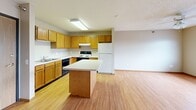 This compact yet efficiently designed one-bedroom, one-bathroom unit makes excellent use of its single-floor layout. The open living area features warm-toned laminate hardwood flooring, neutral beige walls, and a textured ceiling with a ceiling fan, creating a comfortable and airy atmosphere. Natural light filters in through multiple windows fitted with horizontal blinds.

The kitchen is a standout feature, equipped with warm oak cabinetry, a central island with a light-colored countertop ideal for meal prep or casual dining, a stainless steel sink, a dishwasher, a range, and a full-size refrigerator. A skylight above adds a bright, open feel to the space.

The bedroom offers plush wall-to-wall carpeting, a window for natural light, and a textured ceiling, providing a cozy and restful retreat. A dedicated closet with built-in shelving and a hanging rod offers practical storage.

The bathroom is finished with oak cabinetry, a single-sink vanity with a framed mirror, and laminate flooring that ties in with the rest of the unit. An adjacent linen closet with built-in shelving adds to the storage options. Throughout the unit, warm wood-toned doors and trim provide a cohesive, welcoming aesthetic.