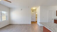 This single-story unit is thoughtfully designed with a clean, modern aesthetic throughout. The open-concept kitchen serves as a central feature, showcasing rich medium-toned wood cabinetry paired with light granite countertops, stainless steel appliances including a range, microwave, and refrigerator, and a kitchen island with a built-in sink — offering both functionality and a natural gathering point. Wood-look plank flooring runs through the main living and kitchen areas, lending a cohesive and easy-to-maintain finish.

The living area is generously sized, illuminated by natural light from windows with blinds and a glass exterior door, and fitted with a ceiling fan overhead. A secondary living or dining space connects seamlessly, also featuring wood-look flooring and a louvered interior door leading to additional rooms. The bedroom is carpeted and receives natural light through a window with blinds, and includes a ceiling fan. The bathroom features a full tub-shower combination, toilet, and wood-look tile flooring. A dedicated laundry area houses a full-size top-load washer and dryer with overhead shelving, completing the unit's practical amenities.