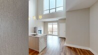 Located in Kansas City's vibrant Crossroads district, this modern two-story residence offers three bedrooms and two bathrooms across two well-appointed floors. The main level is anchored by a dramatic open-plan kitchen and living area beneath soaring double-height ceilings, flooded with natural light from a towering wall of upper-level windows. The kitchen features sleek flat-front cabinetry, stainless steel appliances, a granite-clad waterfall island with an integrated sink, and stylish pendant lighting. The living room showcases warm hardwood flooring, a striking granite-surround fireplace, and oversized floor-to-ceiling windows framing sweeping views of the Kansas City skyline. A contemporary staircase with black metal railings and a wood-capped handrail leads to the upper level, where hardwood flooring continues through the open hallway. The bedrooms offer plush carpeting and generous natural light, with one room featuring exposed industrial ductwork and panoramic city views. The bathrooms are finished with large-format tile and glass-enclosed walk-in showers. Two closets provide practical storage throughout. The overall ambiance is sleek, urban, and sophisticated, blending industrial loft aesthetics with high-end modern finishes.