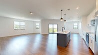 Located in Merriam, Kansas, this thoughtfully designed 2-bedroom, 2-bathroom single-floor residence offers a bright and modern living experience. The open-concept kitchen and living area serves as the heart of the home, showcasing warm hardwood-style flooring throughout, crisp white walls, and an abundance of natural light from multiple black-framed windows. The kitchen is appointed with white shaker cabinetry, a light quartz countertop, a distinctive powder-blue island with a built-in sink, stainless steel appliances, a subway tile backsplash, and stylish pendant lighting. Sliding glass doors lead directly to a private balcony overlooking a scenic outdoor view, seamlessly blending indoor and outdoor living. The spacious primary bedroom features a ceiling fan and direct access to a well-appointed en-suite bathroom complete with a double vanity, illuminated mirror, matte black fixtures, and a glass-enclosed walk-in shower. A generous walk-in closet with wire shelving adds practical storage. The second bedroom is equally well-sized with a ceiling fan and easy access to the second full bathroom. A dedicated laundry room with a full-size washer and dryer rounds out this clean, contemporary residence.