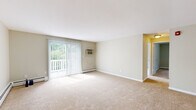 Located at 7 Lathrop Ln in Rocky Hill, Connecticut, this two-bedroom, one-bathroom residence offers a well-organized single-floor layout with a functional and comfortable design throughout. The living room is a generous, open space finished with neutral-toned carpet and anchored by a sliding glass door fitted with vertical blinds, providing direct access to a balcony and allowing abundant natural light and outdoor greenery views. A wall-mounted air conditioning unit and baseboard heating ensure year-round comfort. The galley-style kitchen features white cabinetry, granite-look countertops, tile flooring, and white appliances including a refrigerator, dishwasher, and electric range. The full bathroom is clean and bright, with a tiled mosaic floor, white vanity, and a tub-shower combo. Both bedrooms are carpeted and finished in soft neutral tones. The primary bedroom offers a large sliding-door closet and natural light from a window with outdoor views. The second bedroom also includes a sliding closet and connects conveniently to the hallway. Baseboard heating is present throughout, and the layout is completed by a central hallway connecting all rooms efficiently.