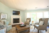 Located at 624 Suhtai Ct in Virginia Beach, VA, this single-story property offers a thoughtfully designed layout with an inviting, coastal-inspired aesthetic throughout. Rich, dark hardwood flooring flows seamlessly across the open living areas, creating a cohesive and polished look.

The main living room is a standout space, anchored by a classic fireplace with a white tile surround and a decorative mantle. Vaulted ceilings with an elegant chandelier add volume and drama, while large windows dressed in patterned drapes flood the room with natural light and provide views of the surrounding greenery. A separate sitting or sunroom area features floor-to-ceiling shuttered French doors, offering a bright and flexible retreat.

The kitchen is functional and well-equipped, featuring rich dark wood cabinetry, ample counter space, stainless steel appliances, and a double sink. Natural light enters through multiple windows, enhancing the room's practicality. The open layout connects the kitchen to the main living and dining areas, ideal for gathering and entertaining.

The overall ambiance of the space is warm and welcoming, blending neutral soft-blue and cream tones with natural textures. The open floor plan and abundant natural light make this property feel spacious, comfortable, and move-in ready.