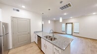 Located at 691 Union Chapel Rd in Cedar Creek, TX, this well-appointed single-story home offers two bedrooms and two bathrooms within a thoughtfully designed open floor plan. The combined kitchen and living area serves as the heart of the home, featuring light luxury vinyl plank flooring, recessed lighting, and a front entry door flanked by sidelight windows that invite natural light into the space. The kitchen is highlighted by a central island with granite countertops and a double stainless steel sink, white shaker cabinetry, and a full suite of stainless steel appliances including a refrigerator, range, microwave, and dishwasher. Elegant pendant lights hang above the island, adding a modern touch. The spacious primary bedroom is carpeted for comfort and includes a ceiling fan, a natural light-filled window, and access to a generously sized walk-in closet with wire shelving and built-in shelving units. The secondary bedroom is equally well-lit with a large window and plush carpeting. Both bathrooms feature clean, functional finishes including a tub-shower combination. A dedicated laundry area with wire shelving provides added convenience, completing this efficient and modern home.