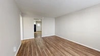 Located at 8765 Ferndale Rd in the Lake Highlands area of Dallas, TX, this single-story, 3-bedroom, 2-bathroom home offers a practical and well-organized layout. The living room serves as the central gathering space, featuring warm wood-look luxury vinyl plank flooring and neutral-toned walls that create a bright, clean atmosphere. A hallway connects the main living areas to the rest of the home, leading to a compact kitchen equipped with white shaker-style cabinetry, a black refrigerator, an electric range, and light LVP flooring — providing efficient use of space. The primary bedroom is generously proportioned and finished with wood-look flooring, while the additional bedrooms feature plush carpeting and dedicated closets, offering ample storage. The two bathrooms are finished with white cabinetry and LVP flooring; one includes a full tub-shower combo with white tile surround, and the other features a clean, minimal layout. Throughout the home, a consistent neutral color palette and white trim contribute to a cohesive, move-in-ready aesthetic. The straightforward single-floor plan ensures easy navigation and accessibility across all rooms.