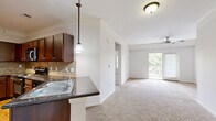 Located at 10505 W 134th St in Overland Park, KS, this one-bedroom, one-bathroom residence offers a well-designed layout that maximizes comfort and functionality. The open-concept kitchen is a standout feature, boasting rich dark-stained cabinetry, dark granite countertops, a tile backsplash, and a full suite of stainless steel appliances including a refrigerator, range, microwave, and dishwasher. A peninsula with a double-basin sink and pendant lighting creates a natural divide between the kitchen and the adjoining living area, which is enhanced by crown molding and a ceiling fan. Plank hardwood-style flooring runs through the kitchen, while plush carpet extends throughout the living room and bedroom. The living area is bright and open, with a sliding glass door providing access to an outdoor space and filling the room with natural light. The generously sized bedroom features dual windows, crown molding, a ceiling fan, and a closet with double doors. The bathroom is well-appointed with a dark granite vanity, rich wood cabinetry, a tiled tub-shower combination, and hardwood-style flooring. Crown molding is carried consistently throughout the home, adding a refined, cohesive touch to the overall aesthetic.