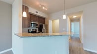 This well-appointed 2-bedroom, 2-bathroom residence is thoughtfully designed across a single floor, offering a comfortable and functional layout. The open-concept kitchen serves as the heart of the home, featuring rich dark-stained cabinetry, gleaming granite countertops, and a large peninsula that doubles as a breakfast bar. Stainless steel appliances, including a microwave, range, and refrigerator, complete the kitchen's modern aesthetic. Pendant lighting above the peninsula and track lighting overhead add both style and practicality to the space. Durable wood-look flooring flows throughout the main living areas, lending warmth and continuity to the design. The open floor plan connects the kitchen seamlessly to the living area, creating a bright and inviting atmosphere ideal for both everyday living and entertaining. A hallway leads to the two well-sized bedrooms, each offering privacy and comfort. With clean lines, neutral tones, and contemporary finishes throughout, this residence presents a polished and move-in-ready living environment suited for a variety of lifestyles.
