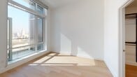 Located at 427 W 5th St in the heart of downtown Los Angeles, this contemporary single-floor residence showcases a clean, modern design with an emphasis on open living and natural light. Light hardwood flooring flows throughout the space, complementing the bright white walls and creating a cohesive, airy atmosphere.

The kitchen is a standout feature, outfitted with rich walnut-toned cabinetry on the lower level contrasted by crisp white upper cabinets. Stainless steel appliances — including a gas range, built-in microwave, refrigerator, and dishwasher — are paired with a white quartz countertop and a subtle tile backsplash. The open layout connects the kitchen seamlessly to the living area, which benefits from floor-to-ceiling windows that frame sweeping downtown Los Angeles skyline views and flood the space with natural light.

A dedicated in-unit laundry closet provides added convenience, housing a stacked washer and dryer behind louvered doors. The bathroom is finished with large-format neutral tiles, a soaking tub with a glass enclosure, and open wood shelving, offering a clean and functional design. The bedroom is generously proportioned with large windows that allow ample sunlight and open outlooks over the city. The overall ambiance is modern, minimal, and well-suited to urban living.