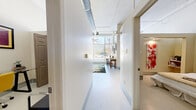 Located at 317 Lexington Avenue in San Antonio, Texas, this one-bedroom, two-bathroom unit showcases an industrial-modern aesthetic with thoughtful design details throughout. The living area immediately impresses with soaring ceilings, exposed galvanized ductwork, and expansive floor-to-ceiling windows that flood the space with natural light and offer open street views. Polished concrete-style flooring runs throughout, complementing the clean, neutral palette of the walls. A ceiling fan adds a practical touch to the bright, airy living space, which connects seamlessly to a bar-height dining area. A hallway leads from the main living area into the private quarters. The generously proportioned bedroom features high ceilings with industrial accents, built-in shelving, and a dedicated closet, creating a comfortable and functional retreat. The unit includes two bathrooms: one with a pedestal sink and walk-in shower, and a second featuring a full soaking tub and shower combo with a modern vanity and ample counter space. The overall ambiance is urban and contemporary, with an open, loft-inspired character that balances industrial architectural elements with a warm, livable atmosphere well-suited to city living in San Antonio.