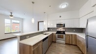 This well-appointed single-floor residence offers three bedrooms, two bathrooms, and a thoughtfully designed layout that maximizes functionality. The open-concept kitchen is a standout feature, showcasing a two-tone design with white upper cabinetry and warm wood-toned lower cabinets, complemented by a mosaic tile backsplash and light quartz countertops. A peninsula with an undermount sink and elegant pendant lighting connects the kitchen seamlessly to the living area, which features durable wood-style flooring and a ceiling fan. Stainless steel appliances, including a refrigerator, range, microwave, and dishwasher, complete the kitchen. The bedrooms offer plush carpeting and are filled with natural light through blinds-covered windows, with ceiling fans adding comfort. The primary bedroom features wood-style flooring and generous window views. The bathrooms are clean and functional with modern fixtures, including a soaking tub. A dedicated in-unit laundry room houses a full-size washer and dryer set with overhead wire shelving. Two closets provide ample storage throughout the home. The overall aesthetic is clean and contemporary, with a neutral color palette, dark wood accents, and consistent modern finishes that create a cohesive, move-in-ready environment.