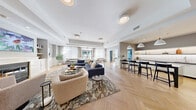 Located at 3000 Taylor Pond Lane in Bedford, MA, this thoughtfully designed single-floor amenity space offers a comprehensive suite of facilities spread across a generously sized footprint. The entrance greets visitors with elegant herringbone hardwood flooring, warm oak-framed glass doors, and a reception area that sets a refined yet welcoming tone throughout.

The expansive main lounge is a standout feature, bathed in natural light from floor-to-ceiling sheer-draped windows and French doors that open to the outdoors. Tray ceilings add architectural depth, while plush seating arrangements and an adjacent bar-height kitchen counter with pendant lighting create a social and comfortable atmosphere.

The sleek kitchen showcases white cabinetry, textured tile backsplash, stone countertops, and herringbone flooring — a polished space designed for communal use. Two well-appointed media rooms offer intimate settings with large-screen televisions, warm ambient lighting, and comfortable lounge seating.

Four private offices provide focused workspaces, each equipped with wall-mounted displays and conference-style furnishings. The two fitness areas are bright and spacious, outfitted with cardio machines, strength equipment, turf zones, wall mirrors, and ample storage. A connecting hallway with patterned carpeting and accent columns ties all areas together cohesively.