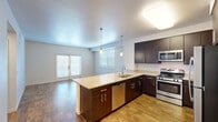 Located at 55 Maria Drive in Petaluma, California, this one-bedroom, one-bathroom residence delivers a well-designed single-floor layout with a clean, contemporary aesthetic throughout. The open-concept kitchen and living area forms the heart of the home, where rich dark-espresso cabinetry contrasts beautifully with light quartz countertops. A peninsula island with pendant lighting serves as both a functional workspace and a casual dining spot. Stainless steel appliances — including a gas range, microwave, and dishwasher — complete the kitchen's modern appeal. Warm hardwood-style flooring flows throughout the living area, which benefits from generous natural light courtesy of sliding glass door access and multiple windows fitted with sleek blinds. The bedroom offers a comfortable, carpeted retreat with a window that brings in natural light, while a dedicated closet provides practical storage. The bathroom features a dark wood vanity with a light countertop, a large mirror, and clean, neutral finishes. A hallway connects the spaces efficiently. The overall ambiance is fresh, modern, and move-in ready, making this Petaluma residence an appealing and functional place to call home.