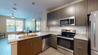 Located at 200 Cedar Pointe Dr in Blacksburg, VA, this well-appointed 2-bedroom, 2-bathroom unit offers a thoughtfully designed layout across a single floor. The open-concept kitchen serves as a central hub, featuring dark wood-tone cabinetry, granite countertops, a subway tile backsplash, and a full suite of stainless steel appliances including a bottom-freezer refrigerator, electric range, over-range microwave, and dishwasher. A peninsula with bar seating and a pendant light above adds both functionality and style, flowing seamlessly into the living area. The living room is bright and comfortable, benefiting from a large window that invites natural light and outdoor views of the surrounding greenery. Light wood-style flooring runs throughout the main living spaces, lending a clean and cohesive aesthetic. Each bedroom is well-sized, with large windows providing ample natural light and views of the outdoors. The primary bedroom is comfortably proportioned and is accompanied by a private bathroom featuring a granite vanity, dark cabinetry, and a full tub-shower combination with white tile surround. Two closets provide practical storage solutions throughout the unit. Ceiling fans in the bedrooms and living area enhance everyday comfort.