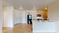 This single-floor residence offers a clean, contemporary design throughout its thoughtfully laid-out interior. The open-concept living and kitchen area serves as the heart of the home, where light hardwood-style flooring extends seamlessly from the entry door through the main living space. The kitchen is well-equipped with light wood flat-panel cabinetry reaching toward the ceiling, providing generous storage. Black appliances — including a full-size refrigerator, range, and over-the-range microwave — offer a sharp contrast against the white quartz countertops. A central kitchen island with an undermount sink and matching white countertop creates a natural hub for meal prep and casual dining.

The bedroom areas feature the same warm hardwood-style flooring and are filled with natural light from large windows fitted with horizontal blinds. One room includes a sliding glass door that opens to the outdoors, as well as a wall-mounted HVAC unit for individual climate control. Additional rooms are bright and versatile, suited for use as bedrooms or a home office.

The bathroom is finished with a decorative patterned tile floor that adds visual interest, paired with a light wood vanity, white quartz countertop, large mirror, and brushed nickel hardware. The overall aesthetic is cohesive, modern, and move-in ready.