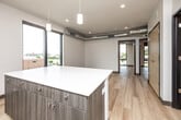 This contemporary 2-bedroom, 2-bathroom unit offers a well-designed open-concept layout spread across a single floor. The combined kitchen and living area serves as the heart of the unit, showcasing large floor-to-ceiling windows that frame urban cityscape views and flood the space with natural light. The kitchen is outfitted with stainless steel appliances — including a range, microwave, dishwasher, and refrigerator — complemented by warm wood-toned cabinetry, white quartz countertops, and a central island with additional storage. Light-toned hardwood flooring runs throughout the entire unit, lending a clean, cohesive aesthetic. Exposed metallic ductwork adds an industrial character that carries through the living area and into the primary bedroom. The primary bedroom benefits from its own floor-to-ceiling window with city views, a walk-in closet, and direct access to a private en-suite bathroom. The second bedroom is a well-proportioned room with a built-in closet and its own access to the second bathroom. Both bathrooms feature light wood flooring consistent with the rest of the unit. A hallway connects the bedrooms and bathrooms, completing the efficient and modern floor plan.
