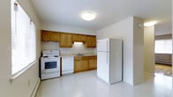 This multi-floor space spans three levels, offering a well-organized and functional layout throughout. The kitchen is a standout feature, designed with practicality in mind. It showcases a row of warm-toned wood cabinetry that lines the walls, providing ample storage for everyday needs. The cabinetry is complemented by a clean countertop workspace and an undermount sink, making meal preparation straightforward and efficient. White appliances, including a freestanding electric range, a dishwasher, and a full-size refrigerator, complete the kitchen ensemble and contribute to the space's bright, cohesive aesthetic. The light-toned tile flooring reflects natural and overhead lighting, enhancing the sense of openness in the kitchen area. Flush-mount ceiling lighting keeps the space well-illuminated throughout. The overall ambiance across the three floors is clean and understated, with neutral wall tones that lend a versatile backdrop suitable for a variety of uses. The straightforward design prioritizes functionality and ease of use, making this a practical space well-suited for everyday living across its multiple levels.