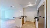Located in the heart of Los Angeles on W 6th Street, this modern one-bedroom, one-bathroom residence offers a thoughtfully designed layout with clean lines and a bright, contemporary aesthetic throughout. Light wood flooring flows seamlessly through the open-concept kitchen and living area, creating a cohesive and airy feel. The kitchen is well-appointed with white cabinetry, dark countertops, a subway tile backsplash, and a full suite of stainless steel appliances including a gas range, microwave, dishwasher, and refrigerator. A central peninsula with a pendant light overhead provides additional counter space and a natural focal point for the living area. The bedroom is carpeted for comfort, receives natural light through a window framing views of tropical greenery, and is complemented by a dedicated walk-in closet with built-in shelving for ample storage. The full bathroom features wood-tone flooring, a dark-countered vanity with white cabinetry, and a tub-shower combination. Recessed lighting throughout maintains a clean, modern look, while the neutral white walls provide a versatile backdrop. A louvered closet door near the entry adds a refined architectural touch to this well-planned urban residence.