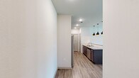 This thoughtfully designed 2-bedroom, 2-bathroom single-floor residence offers a functional and modern living experience. The open-concept kitchen is a standout, featuring dark espresso cabinetry, granite countertops, a large center island, and a full suite of stainless steel appliances including a side-by-side refrigerator, electric range, built-in microwave, and dishwasher. Striking pendant lights hang above the island, complementing the wood-look luxury vinyl flooring that flows seamlessly into the living area. The living space is bright and airy, benefiting from multiple windows and a glass-panel door that invites natural light, with a ceiling fan adding comfort overhead. Both bedrooms feature plush carpeting, and the primary bedroom includes direct access to an en suite bathroom equipped with a walk-in shower with tile surround, as well as a dedicated walk-in closet with built-in shelving. The second bathroom offers a tiled soaking tub and shower combination with a granite-topped vanity. A dedicated in-unit laundry room accommodates a full-size washer and dryer with overhead shelving for added storage. Two closets throughout the unit enhance organizational options, completing this well-rounded and move-in-ready residence.
