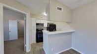 This efficiently designed one-bedroom, one-bathroom unit makes excellent use of its single-floor layout, offering a cohesive and functional living space. The open-concept kitchen is equipped with white cabinetry, light countertops, and a full suite of black appliances, including a range, refrigerator, and dishwasher. A white peninsula counter extends into the living area, providing additional workspace and a natural division between cooking and living zones. Wood-look flooring runs throughout the kitchen and main living areas, lending a clean, modern aesthetic.

The living room is bright and inviting, highlighted by a set of French doors with slatted blinds that allow ample natural light and offer views of the surrounding neighborhood. Soft carpeting continues into the bedroom, which features a dedicated walk-in closet with hanging rods for generous storage. A ceiling fan is visible from the bedroom doorway, enhancing comfort throughout.

The bathroom is clean and straightforward, featuring a white vanity with a light countertop, overhead cabinetry for storage, a toilet, and a full tub-shower combination with white tile surround and wood-look flooring. Neutral tones and a textured ceiling throughout the unit create a consistent, understated palette that is both practical and easy to personalize.