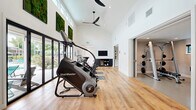 Located at Portage Bay in Davis, California, this well-appointed fitness center offers a comprehensive workout facility across a single floor. The space is designed with a bright, open aesthetic, featuring soaring vaulted ceilings, crisp white walls, and light wood-style flooring that create an energizing and welcoming environment.

The main exercise room is the centerpiece of the facility, benefiting from an abundance of natural light through floor-to-ceiling glass doors that open to an outdoor pool area, as well as a row of clerestory windows positioned high on the walls. Decorative preserved moss wall art adds a vibrant, organic touch to the clean interior. Cardio equipment including a StairMaster, Peloton spin bikes, a treadmill, and a rowing machine are thoughtfully arranged throughout, accompanied by a mounted flat-screen television and a ceiling fan overhead.

A second, dedicated strength-training room provides a focused space for resistance work, housing a Smith machine, a weight bench, a dumbbell rack, and yoga mat storage. This room features its own recessed lighting and window for natural ventilation.

The facility also includes a clean, ADA-accessible full bathroom finished with large-format neutral tiles. Two entry points provide convenient access to the space, completing this fully equipped, community fitness destination.