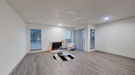 This single-story, 2-bedroom, 2-bathroom residence offers a thoughtfully designed layout that makes efficient use of its space. Throughout the unit, light grey wood-look flooring provides a cohesive, contemporary aesthetic that ties each room together.

The living room serves as the centerpiece of the home, featuring a classic fireplace flanked by multiple windows with slatted blinds that invite natural light. A sliding glass door adds additional brightness and outdoor access, enhancing the open feel of the space. Recessed lighting and a textured ceiling complete the room.

The galley-style kitchen is equipped with white shaker cabinetry, sleek white countertops, a stainless steel sink, and a black refrigerator. A set of double bi-fold doors provides convenient pantry or closet storage.

Both bedrooms are comfortably proportioned and feature windows with blinds, offering natural light and privacy. The primary bedroom includes a ceiling fan and vertical blinds. Each bathroom mirrors the home's modern aesthetic, showcasing grey shaker vanity cabinets, white quartz countertops, large mirrors, and wood-look flooring, creating clean, functional spaces throughout.