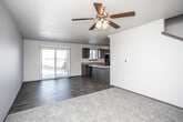 This two-floor residence is designed with a practical, open layout that connects the main living and kitchen areas seamlessly. The kitchen is outfitted with dark espresso-toned cabinetry, light-colored countertops, and black appliances including a range, over-the-range microwave, and refrigerator. A peninsula counter extends into the living space, providing additional prep space and a casual dining option. The main level features a combination of dark hardwood-style flooring and carpeted areas, with a textured ceiling throughout. A sliding glass patio door floods the living area with natural light and provides outdoor access, while a ceiling fan with an integrated light fixture enhances comfort. A staircase leads to the upper level, where carpeted bedrooms feature windows with blinds that allow natural light. Bathrooms are found on both levels; one includes a tub-shower combo, light tile flooring, a dark vanity with a light countertop, and a window for ventilation, while another offers a similar vanity setup with additional storage. The overall aesthetic is clean and functional, with neutral tones and consistent dark cabinetry creating a cohesive look throughout.