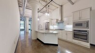 Located in Milwaukee's vibrant Historic Third Ward, this single-floor loft at 226 N Water St masterfully blends industrial character with modern refinement. Soaring ceilings, exposed ductwork, and original ornate columns set a dramatic architectural tone throughout, while polished concrete floors reflect natural light and unify each space.

The open-concept kitchen is a true centerpiece, featuring crisp white shaker cabinetry, light blue subway tile backsplash, marble-veined granite countertops, a generous island with seating, stainless steel appliances including a gas cooktop, wall oven, built-in microwave, and French door refrigerator, all topped by globe pendant lighting.

The living area extends generously from the kitchen, with industrial-steel grid windows flooding the space with natural light and views of the surrounding cityscape. A ceiling fan adds comfort to the expansive room.

The primary bathroom is spa-like, offering a spacious walk-in glass-enclosed shower with large-format white tile, dual vanities with dark granite countertops, white shaker cabinetry, and polished concrete floors. An organized walk-in closet with built-in shelving, drawers, and hanging rods offers excellent storage. An in-unit laundry room with a full-size washer and dryer and upper cabinetry adds everyday convenience.