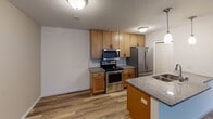 This single-floor residence offers a thoughtfully designed open-concept layout that seamlessly connects the kitchen, dining, and living areas. The kitchen is a functional centerpiece, featuring warm wood cabinetry, granite-style countertops, a subway tile backsplash, stainless steel appliances including a range, over-the-range microwave, and refrigerator, as well as a peninsula with pendant lighting and a built-in sink — ideal for both meal preparation and casual dining. The expansive living area is bathed in natural light from large sliding glass doors that open to a private balcony with outdoor views, complemented by a wall-mounted air conditioning unit and baseboard heating. Hardwood-style flooring flows consistently throughout the main living spaces, adding warmth and visual continuity. The bedroom is generously sized, featuring a ceiling fan with light, a large window with vertical blinds for natural light and privacy, and baseboard heating. The bathroom includes a full-surround shower and tub combination with built-in corner shelving for added convenience. Textured ceilings are present throughout, and the overall color palette of neutral whites and warm beiges creates a clean, welcoming ambiance well-suited for comfortable everyday living.