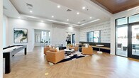 Located at 12100 N Mountain Centre Rd in Marana, Arizona, this thoughtfully designed single-floor space blends contemporary aesthetics with warm Southwestern character. The open-concept living room serves as the heart of the space, showcasing herringbone-patterned hardwood flooring, tray ceilings with recessed lighting, and a striking wood-paneled ceiling accent. A bold black marble fireplace anchors one wall, while large black-framed windows frame picturesque views of native saguaro cacti and vibrant desert landscaping, flooding the interior with natural light. Comfortable tan leather seating arranged around a cowhide area rug creates an inviting lounge atmosphere, complemented by a long upholstered banquette and side tables along the window wall. A distinctive gold sunburst wall sculpture and modern sputnik chandelier add artistic flair. The kitchen is equally refined, featuring dark cabinetry with sleek hardware, dramatic black marble countertops, open floating shelves, and a central island. Black-framed glass doors lead to an outdoor patio area, seamlessly connecting the interior to the surrounding desert environment. Throughout, the space maintains a cohesive, upscale ambiance suited for gathering and socializing.