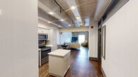 Located at 320 Andrew Higgins Drive in New Orleans' vibrant Warehouse District, this 2-bedroom, 2-bathroom unit masterfully combines historic industrial character with contemporary finishes. Throughout the space, exposed wooden ceiling beams and rich hardwood flooring create a warm, distinctive aesthetic that pays homage to the building's storied past.

The living room is an architectural highlight, featuring a dramatic exposed brick accent wall, soaring beamed ceilings, and a bright window that draws in natural light. The kitchen is well-appointed with white shaker cabinetry, white quartz countertops, a tiled backsplash, stainless steel appliances including a refrigerator, range, microwave, and dishwasher, plus a central island for added prep space.

The primary bedroom offers a comfortable retreat with rustic wood beam ceilings, a double closet, and a clerestory window, while the second bedroom shares similar character-rich detailing. Both bathrooms are finished in clean, neutral tones with tiled showers, and one bathroom conveniently houses a stacked washer and dryer. The layout also includes a dedicated entrance and living area, making this a highly functional and characterful space in the heart of New Orleans.