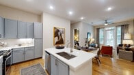 This thoughtfully designed single-story residence showcases a cohesive contemporary aesthetic defined by light hardwood flooring, recessed lighting, and a neutral color palette accented with warm tones. The open-concept kitchen serves as a central hub, featuring a large island with a undermount sink, crisp white quartz countertops, gray shaker-style cabinetry, subway tile backsplash, and a full suite of stainless steel appliances including a gas range, microwave, and French door refrigerator. The kitchen flows seamlessly into the dining and living areas, where large windows and a glass door flood the space with natural light and provide outdoor views.

The living room offers a welcoming atmosphere with sage-gray walls, generous wall space for artwork, and access to a balcony. The bedrooms are distinctly styled, each offering walk-in closets with built-in shelving. One bedroom features warm taupe walls and a large window with outdoor views, while another presents a dramatic dark accent wall with direct access to an en-suite bath. The bathrooms are well-appointed with white cabinetry, quartz vanity tops, large-format tile flooring, and either a glass-enclosed shower or soaking tub combo, providing both comfort and practicality.