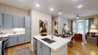 This thoughtfully designed single-story residence showcases a cohesive contemporary aesthetic defined by light hardwood flooring, recessed lighting, and a neutral color palette accented with warm tones. The open-concept kitchen serves as a central hub, featuring a large island with a undermount sink, crisp white quartz countertops, gray shaker-style cabinetry, subway tile backsplash, and a full suite of stainless steel appliances including a gas range, microwave, and French door refrigerator. The kitchen flows seamlessly into the dining and living areas, where large windows and a glass door flood the space with natural light and provide outdoor views.

The living room offers a welcoming atmosphere with sage-gray walls, generous wall space for artwork, and access to a balcony. The bedrooms are distinctly styled, each offering walk-in closets with built-in shelving. One bedroom features warm taupe walls and a large window with outdoor views, while another presents a dramatic dark accent wall with direct access to an en-suite bath. The bathrooms are well-appointed with white cabinetry, quartz vanity tops, large-format tile flooring, and either a glass-enclosed shower or soaking tub combo, providing both comfort and practicality.
