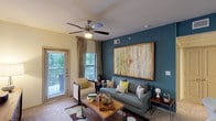 This single-floor, one-bedroom, one-bathroom residence offers a thoughtfully designed layout that maximizes both comfort and functionality. A signature teal accent wall flows consistently throughout the unit, creating a unified and visually striking design theme from the living area to the bedroom.

The living room serves as the heart of the home, featuring a ceiling fan with light fixture, plush carpeting, and multiple windows dressed with patterned drapes that invite ample natural light. A private exterior door provides direct outdoor access, enhancing the sense of openness. The space comfortably accommodates a full seating arrangement centered around a wooden coffee table.

The kitchen is outfitted with rich dark-espresso cabinetry, granite-style countertops, hardwood-style flooring, and a full suite of black appliances including a refrigerator, range, and built-in microwave. Generous upper and lower cabinet storage makes the kitchen both practical and stylish.

The bedroom continues the teal accent wall motif and is generously sized to accommodate a full bedroom set. Two windows allow for natural light and outdoor views, while a ceiling fan adds comfort. A walk-in closet is accessible directly from the bedroom.

The bathroom features a dark-espresso vanity with granite-style countertop, a large mirror, and a shower-tub combination, maintaining the refined aesthetic found throughout the residence.