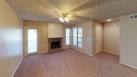 This single-story home offers a well-organized layout with comfortable, functional living spaces throughout. The main living area is generously sized, featuring plush wall-to-wall carpeting, a ceiling fan with light fixture, and a textured ceiling. A standout brick fireplace with a wood-paneled surround serves as the focal point of the room, flanked by windows that bring in natural light. The open layout connects seamlessly to a secondary living or dining space, also carpeted and illuminated by a matching ceiling fan.

The kitchen is laid out in a galley style, featuring warm wood cabinetry, light countertops, hardwood-style flooring, and black appliances including a full-size refrigerator and dishwasher. A pass-through counter opens the kitchen to the main living area, enhancing the sense of connectivity.

The bedrooms are well-proportioned, each equipped with ceiling fans and plush carpeting. Multiple bedrooms feature French doors that open to the outdoors, offering convenient access and natural light. Closet storage is present in the bedrooms as well.

The bathrooms include tub and shower combinations with tiled surrounds, hardwood-style flooring, and wood cabinetry. One bathroom features a compartmentalized layout for added privacy. Throughout the home, textured ceilings and neutral tones create a cohesive and understated aesthetic.