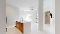 Located in Birmingham, MI, this modern residence offers a thoughtfully designed open-concept layout with clean lines and a bright, contemporary aesthetic throughout. The interior is finished with large-format glossy white tile flooring that reflects abundant natural light, contributing to an airy and expansive feel.

The kitchen serves as a focal point of the living area, anchored by a generous island with a crisp white quartz countertop and an undermount sink with a professional-style faucet. Cabinetry combines warm wood tones with white uppers, and the space is equipped with a full suite of stainless steel appliances, including a gas range, built-in microwave, and French door refrigerator. Recessed lighting and a ceiling fan overhead enhance the open living area adjacent to the kitchen.

The bedroom features high ceilings, polished tile flooring, a warm wood wardrobe, and a wall-mounted television, with a window allowing natural light to filter in. A textured accent wall in soft gray adds a sophisticated design element.

Both bathrooms are finished in crisp white tile and include frameless sliding glass shower enclosures with linear drains and contemporary fixtures, conveying a clean, spa-like atmosphere.

An outdoor terrace with glass-panel railings offers open views of the Birmingham cityscape, providing a compelling outdoor retreat above the urban surroundings.