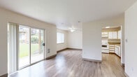 This single-floor home offers five bedrooms and two full bathrooms across a well-organized layout connected by two hallways. The combined kitchen and living room forms the heart of the home, with the living area featuring durable hardwood-style flooring, a ceiling fan, and a sliding glass door that opens to a lush green outdoor space, filling the room with natural light and providing easy exterior access. The kitchen is equipped with ample white cabinetry accented by wood trim, granite-style countertops, a full suite of white appliances including a refrigerator, electric range, and dishwasher, all set atop matching hardwood-style flooring beneath a skylight-style overhead fixture. The five bedrooms offer a comfortable and functional design; several feature plush carpeting, baseboard heating, and windows with views of greenery, while others feature hardwood-style floors and neutral wall tones. The primary bedroom provides a well-proportioned, private retreat. Both bathrooms are consistently appointed with hardwood-style flooring, a granite-style vanity, and a full shower-tub combination with chrome fixtures. The home's clean, neutral palette and practical layout make it a versatile and accommodating space.
