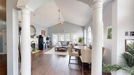 Located at Teal Landing in O'Fallon, Missouri, this single-floor clubhouse offers a thoughtfully designed communal space that combines classic architectural details with a warm, inviting atmosphere. The main living area commands immediate attention with its dramatically vaulted ceilings, accentuated by a decorative chandelier and soft gray walls that lend an airy, open feel. Rich hardwood-style flooring flows throughout, grounding the space with warmth and continuity.

Stately white columns define the transition between the entry and the main lounge, where a cozy fireplace serves as a focal point beneath a wall-mounted television and a decorative round mirror. A coffee station nearby adds a welcoming, community-oriented touch. French doors at the rear of the lounge flood the space with natural light and provide views of the outdoor surroundings.

A round dining table with upholstered chairs occupies one side of the main room, ideal for casual gatherings, while arched windows with transoms add architectural elegance. A separate conference or meeting room features a sleek, modern pendant fixture above a large dining table surrounded by tufted leather chairs, bathed in natural light from multiple windows. A staircase with white-painted balusters connects to additional areas, completing this well-appointed community hub.
