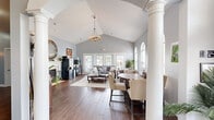 Located at Teal Landing in O'Fallon, Missouri, this single-floor clubhouse offers a thoughtfully designed communal space that combines classic architectural details with a warm, inviting atmosphere. The main living area commands immediate attention with its dramatically vaulted ceilings, accentuated by a decorative chandelier and soft gray walls that lend an airy, open feel. Rich hardwood-style flooring flows throughout, grounding the space with warmth and continuity.

Stately white columns define the transition between the entry and the main lounge, where a cozy fireplace serves as a focal point beneath a wall-mounted television and a decorative round mirror. A coffee station nearby adds a welcoming, community-oriented touch. French doors at the rear of the lounge flood the space with natural light and provide views of the outdoor surroundings.

A round dining table with upholstered chairs occupies one side of the main room, ideal for casual gatherings, while arched windows with transoms add architectural elegance. A separate conference or meeting room features a sleek, modern pendant fixture above a large dining table surrounded by tufted leather chairs, bathed in natural light from multiple windows. A staircase with white-painted balusters connects to additional areas, completing this well-appointed community hub.