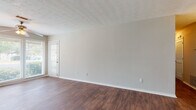 This single-floor residence offers a clean, functional layout with a cohesive design language carried throughout. Rich, dark hardwood-style flooring flows continuously across the living areas, dining space, bedrooms, and bathroom, providing a warm and unified aesthetic.

The living room is a generously sized, open area featuring a textured ceiling, a ceiling fan, and large windows dressed with horizontal blinds that allow abundant natural light to fill the room. A front-facing door provides direct access to the outdoors.

Adjacent to the living room, the dining area is illuminated by a pendant light fixture and connects seamlessly to the kitchen. The kitchen is equipped with deep-toned wood cabinetry, stone-finish countertops offering ample prep space, a stainless steel sink with window view, and a black dishwasher.

The bedrooms are well-proportioned, featuring neutral gray walls, large windows with outdoor views, and practical closet storage with built-in rod systems. Each room benefits from good natural light and a calm, neutral color palette.

The bathroom includes a full tub and shower combo with tiled surround, a toilet, and a vanity with dark wood cabinetry, all set on matching hardwood-style flooring. The overall ambiance of the space is clean, bright, and move-in ready.