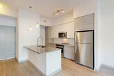Located at 1402 S Dixie Hwy in Lantana, Florida, this well-appointed one-bedroom, one-bathroom residence offers a thoughtfully designed open-concept floor plan. Light wood-look tile flooring flows throughout the entire space, complementing the bright, neutral color palette and creating a cohesive, modern aesthetic.

The kitchen is a standout feature, showcasing a central island with granite countertops and an undermount sink, crisp white cabinetry, stainless steel appliances including a refrigerator, electric range, and built-in microwave, plus a subway tile backsplash. Stylish pendant lights illuminate the island, while track lighting adds additional brightness. The kitchen opens seamlessly into the combined dining and living area, which is bathed in natural light from sliding glass doors and features a ceiling fan overhead.

The generously sized bedroom offers ample space and connects to closets providing practical storage. A versatile den with built-in shelving adds flexible living space. The bathroom includes a full tub-shower combination finished with neutral tile surround. Additional conveniences include a dedicated laundry area and utility room. The private patio, enclosed by a metal railing, offers pleasant outdoor views of the landscaped surroundings and Florida's sunny skies.
