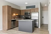 Unit 304 at 225 Portland Ave in Minneapolis, MN is a thoughtfully designed 430-square-foot studio apartment on the third floor. The open-concept layout seamlessly connects the kitchen and living area, all finished with light-toned hardwood-style flooring throughout. 

The kitchen is a standout feature, equipped with stainless steel appliances including a range, microwave, refrigerator, and dishwasher. Warm wood cabinetry extends from floor to ceiling, complemented by white quartz countertops, a gray tile backsplash, a double-basin sink, and a central island that provides additional prep space and storage. An in-unit stacked washer and dryer is also conveniently located off the kitchen.

The living area is bright and airy, benefiting from expansive floor-to-ceiling windows that frame views of the surrounding Minneapolis cityscape and greenery, allowing abundant natural light to fill the space. Two closets provide ample storage within the unit.

The bathroom features light wood-style flooring consistent with the rest of the unit, a wood-toned vanity, and a full tub/shower combination with white tile surround and a matte black shower rod. The neutral warm-gray wall tones throughout the unit create a clean, modern aesthetic that is both inviting and functional.